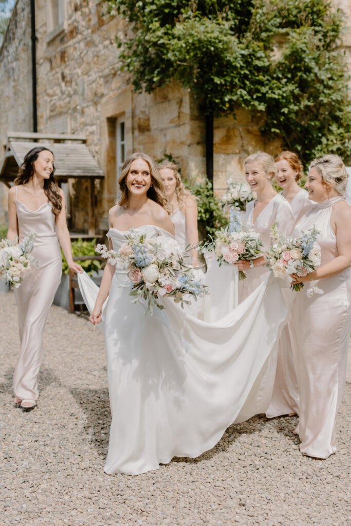 bride in a half penny dress walking to ceremony with her bridesmaids in blush pink silk dresses with fresh natural makeup